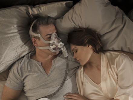 La pareja duerme en una cama. El hombre utiliza la mascarilla facial Versatile AirFit F20