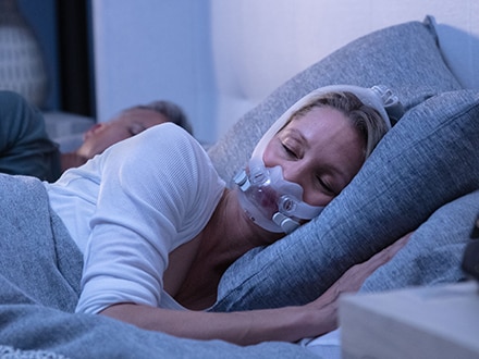 La pareja duerme en una cama. La mujer utiliza una mascarilla facial AirFit F30i que permite total libertad de movimiento.