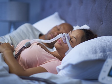 La pareja duerme en una cama. Una mujer utiliza la versátil mascarilla nasal AirFit N20 de ResMed