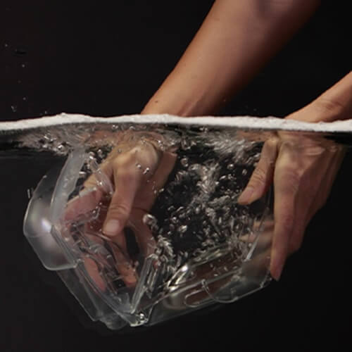 Un par de manos sumergen una lengüeta de humidificador CPAP en un depósito transparente de agua.