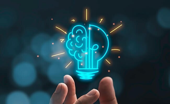 Las yemas de los dedos de alguien que sostiene una bombilla de dibujos animados, superpuestas en la imagen, representan la innovación científica.