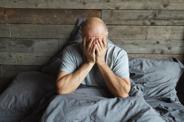  Hombre sentado en la cama con dificultades para dormir.