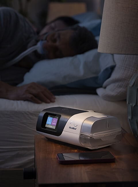 Un paciente con apnea del sueño durmiendo con una máquina CPAP AirSense 11 en la mesilla de noche.